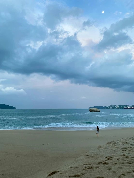 a person standing in the sand on a beach under cloudy skies