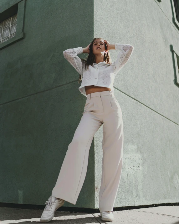 a woman in a white top, cream pants and heels with her arms on the head