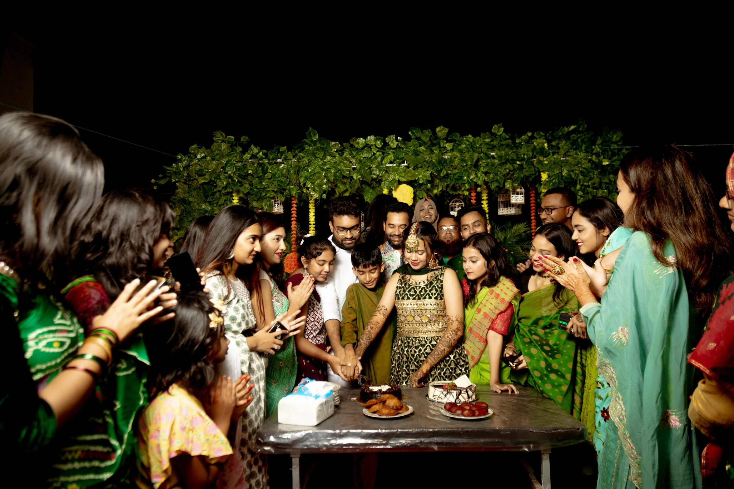 a group of people standing around a table with cake on it