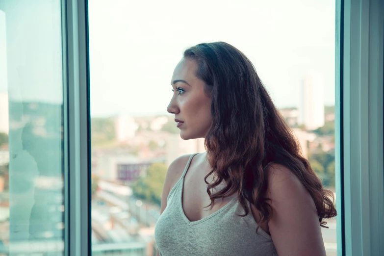 a girl standing near a window looking outside