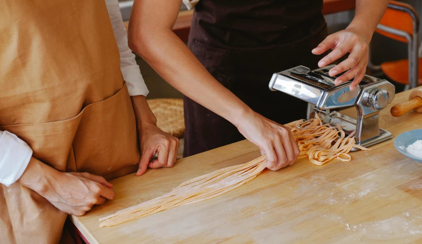 the person is using a pasta cutter to make spaghetti