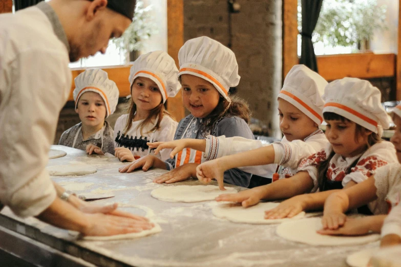 a man wearing a white hat preparing pies for children