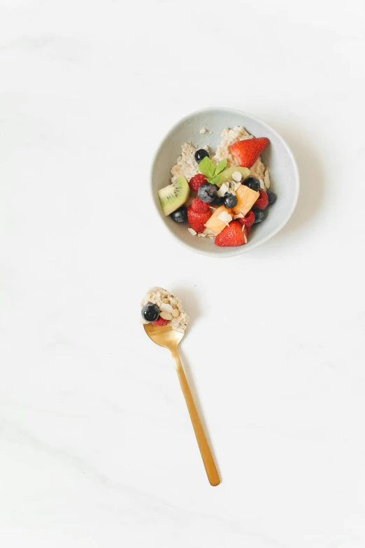 bowl of fruit, oranges, kiwi and other fruit in it next to a wooden spoon