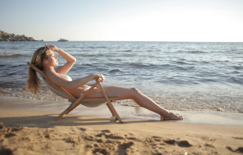 woman posing on a beach while sitting in a lawn chair