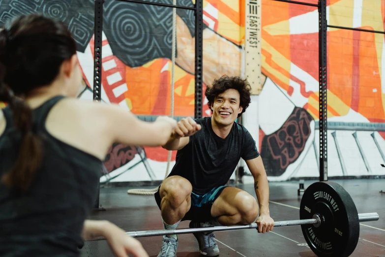 man squatting with one hand on another with a barbell