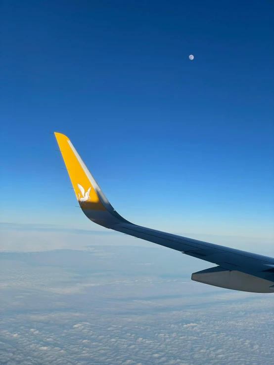 an airplane wing flying above the clouds with a moon