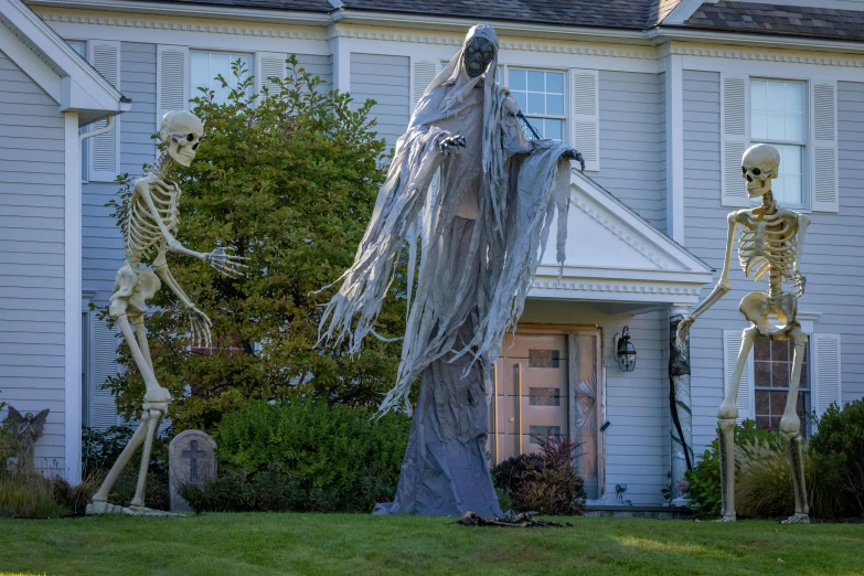 two halloween skeletons dressed as ghost and a skeleton dressed man in front of a white house