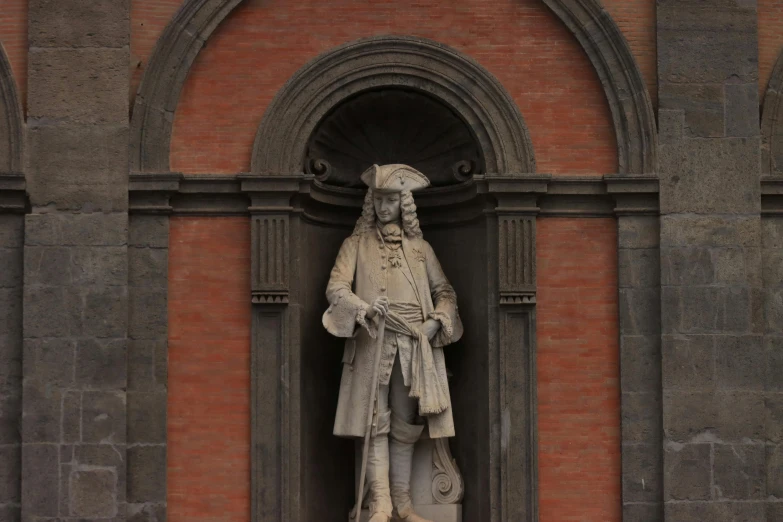 a white statue on a brown building next to a red wall