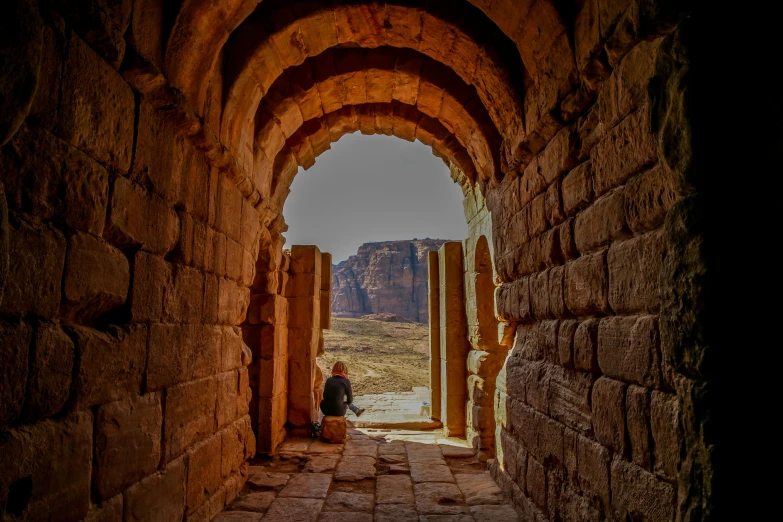 a woman sitting at an old looking doorway in a stone and stone arch