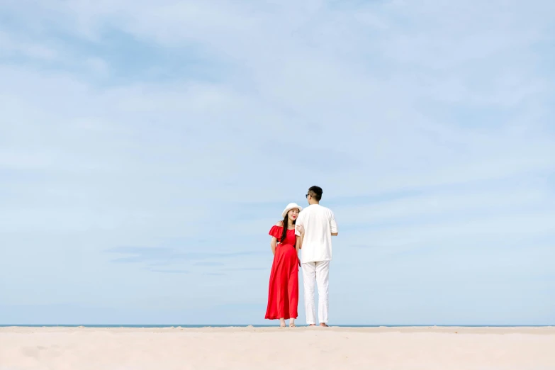 a couple stands together on a beach under a blue sky