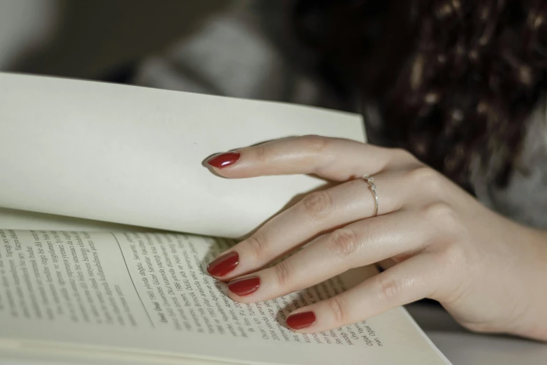 a close up of a person with a red manicure reading a book