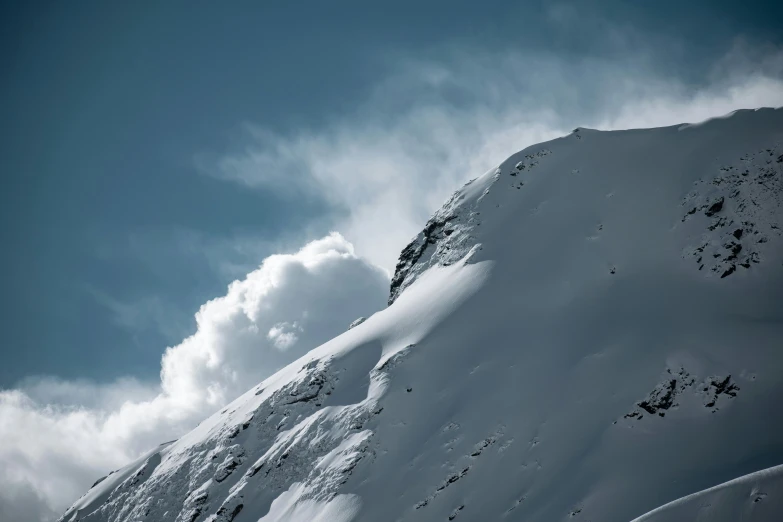 a very tall snow covered mountain side with clouds