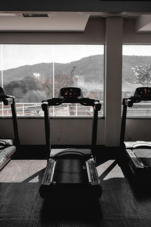 a gym room with two treadmills and two windows