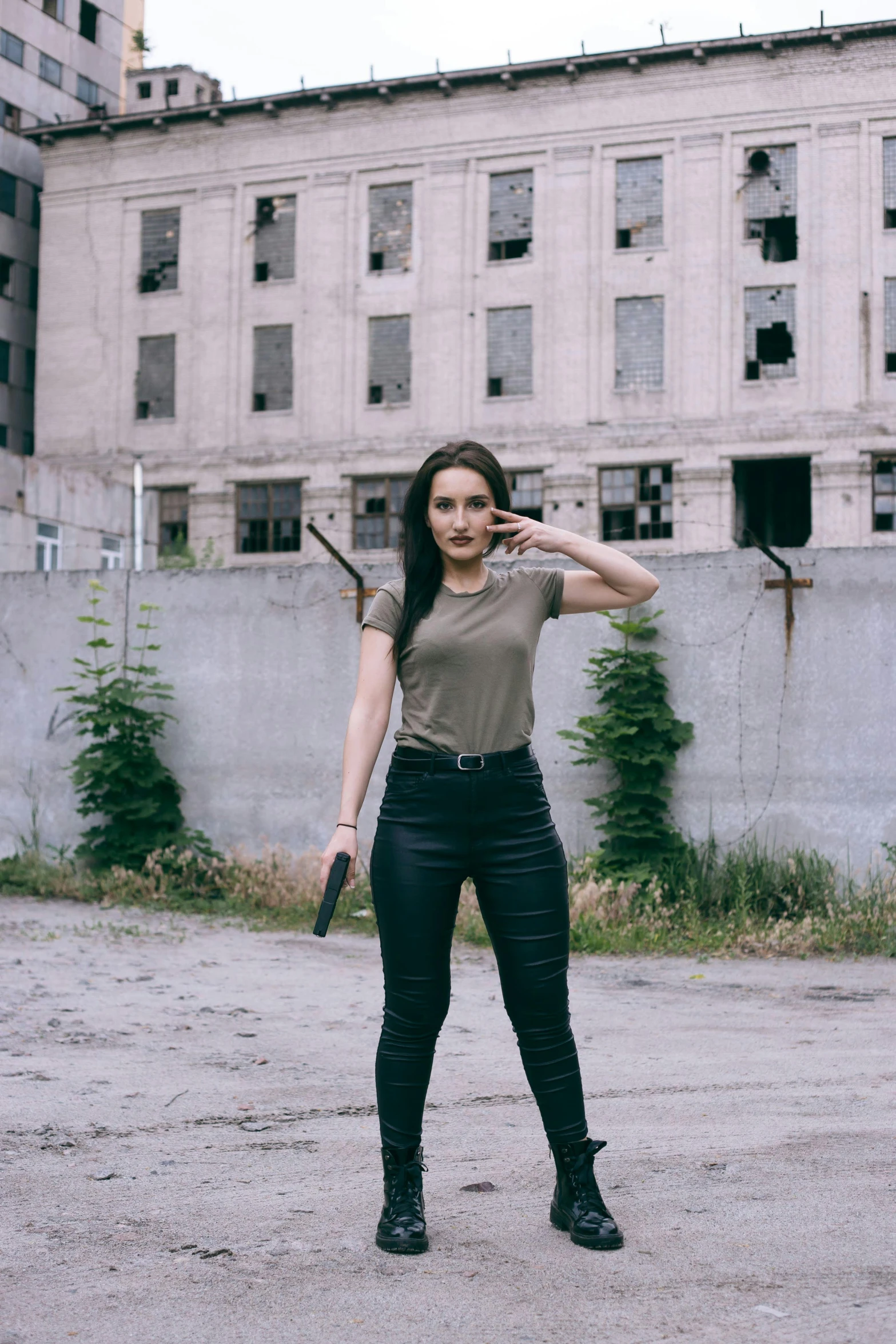 a woman in black pants and brown shirt poses with a gun