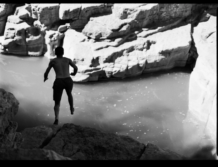 man jumping off cliff into water near rocky terrain