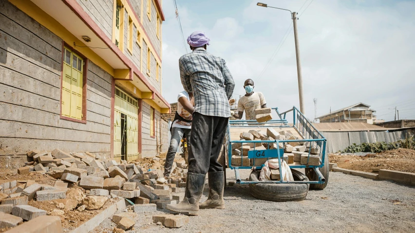 two men work on cement with a blue cart in front of them