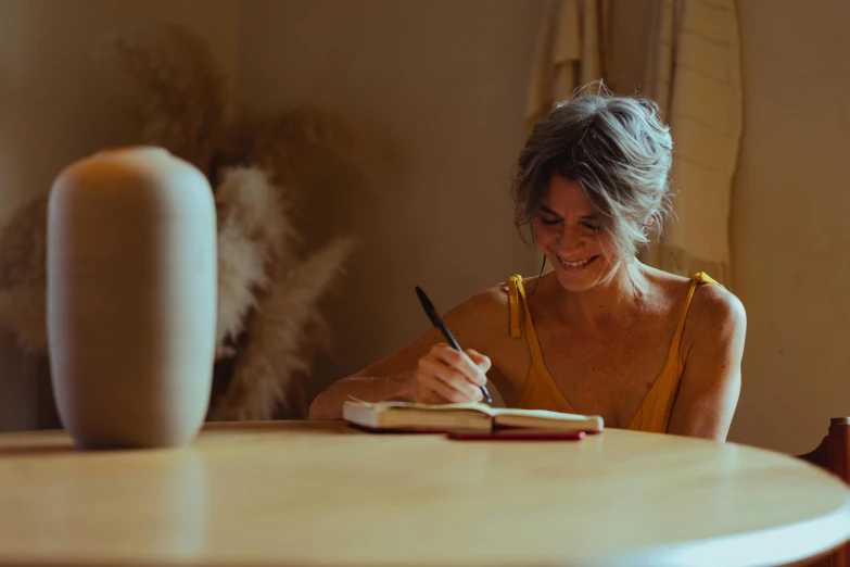 a woman sitting at a table writing on a notebook