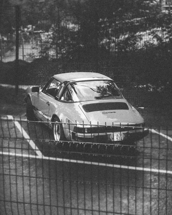 a white car driving down the street past a fence