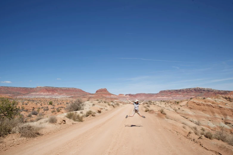 a man stands on a desert road, holding his arms up in the air