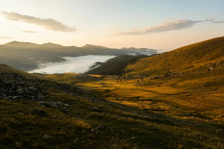 fog covering the mountains above a valley of grassy plains