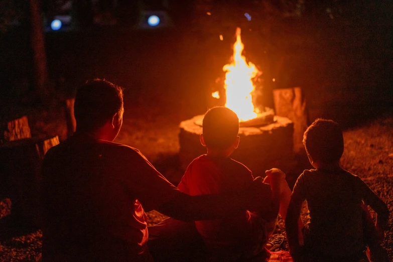 two boys sit together, around an open fire