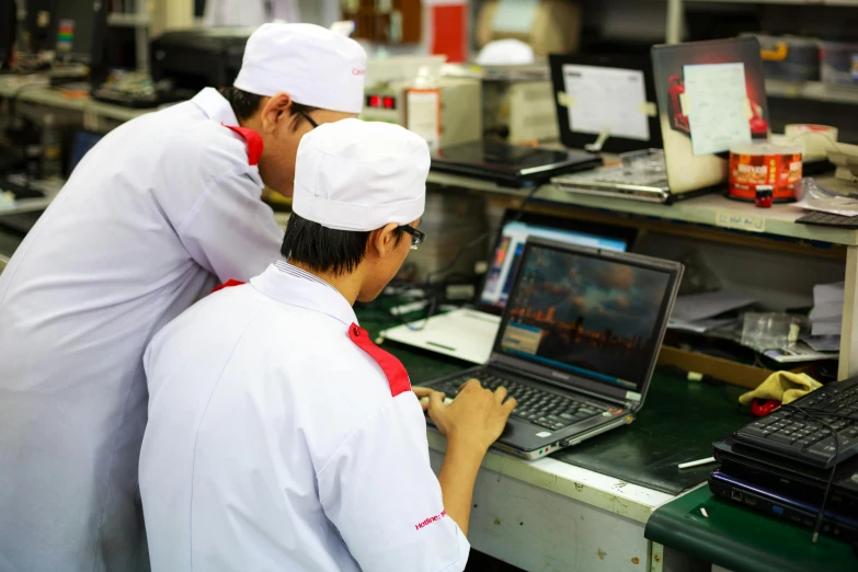 two chefs are looking at an open laptop