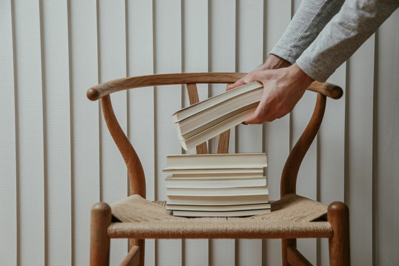 there is a man reaching for stacks of books on the back of a chair