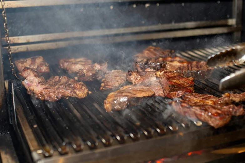 a bbq filled with steaks and a grill tong