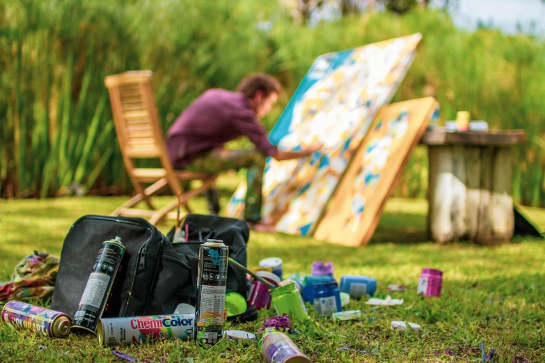 a man sitting in a chair painting with his feet on the grass