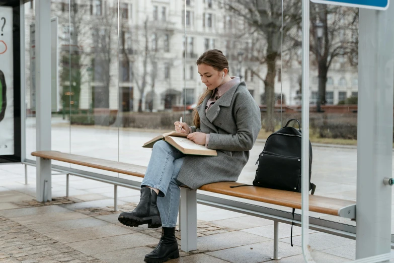 the woman is sitting on the bench with her back pack reading a book