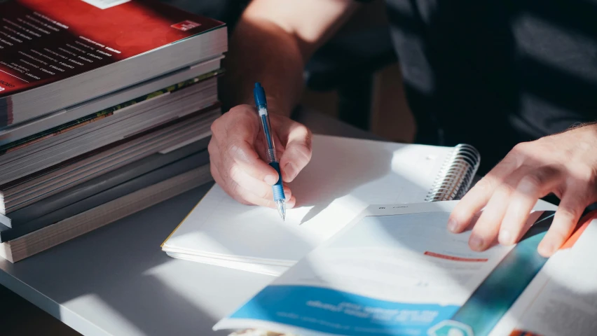 a person writes while doing homework on top of a stack of books