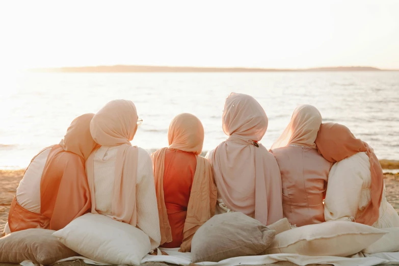 three women in hijabs sit on beach under a blanket