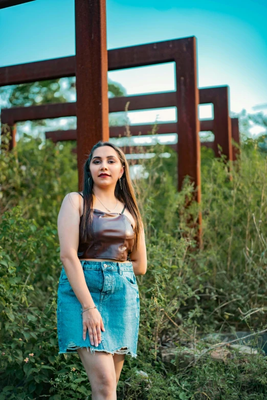 a woman is posing by a rusty structure in a field