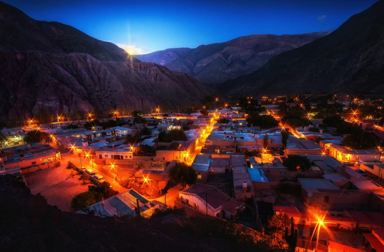 a city is lit up at night next to mountains