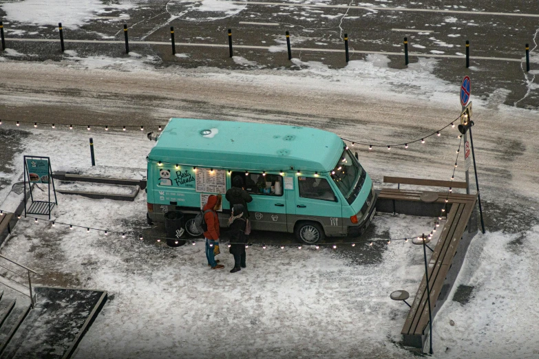 two people stand outside a food truck, dressed in winter clothing, and looking over the snow covered ground