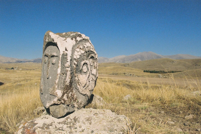 a stone with an image of a face carved into it in a dry grass field