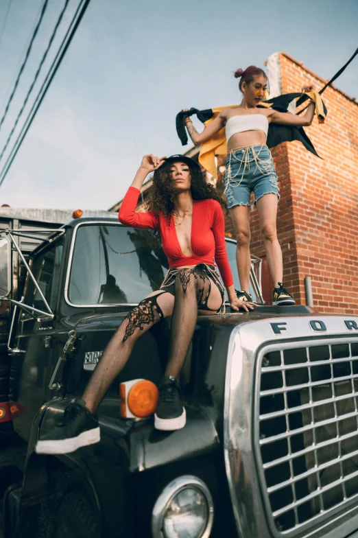 two young women sitting on the hood of a pickup truck