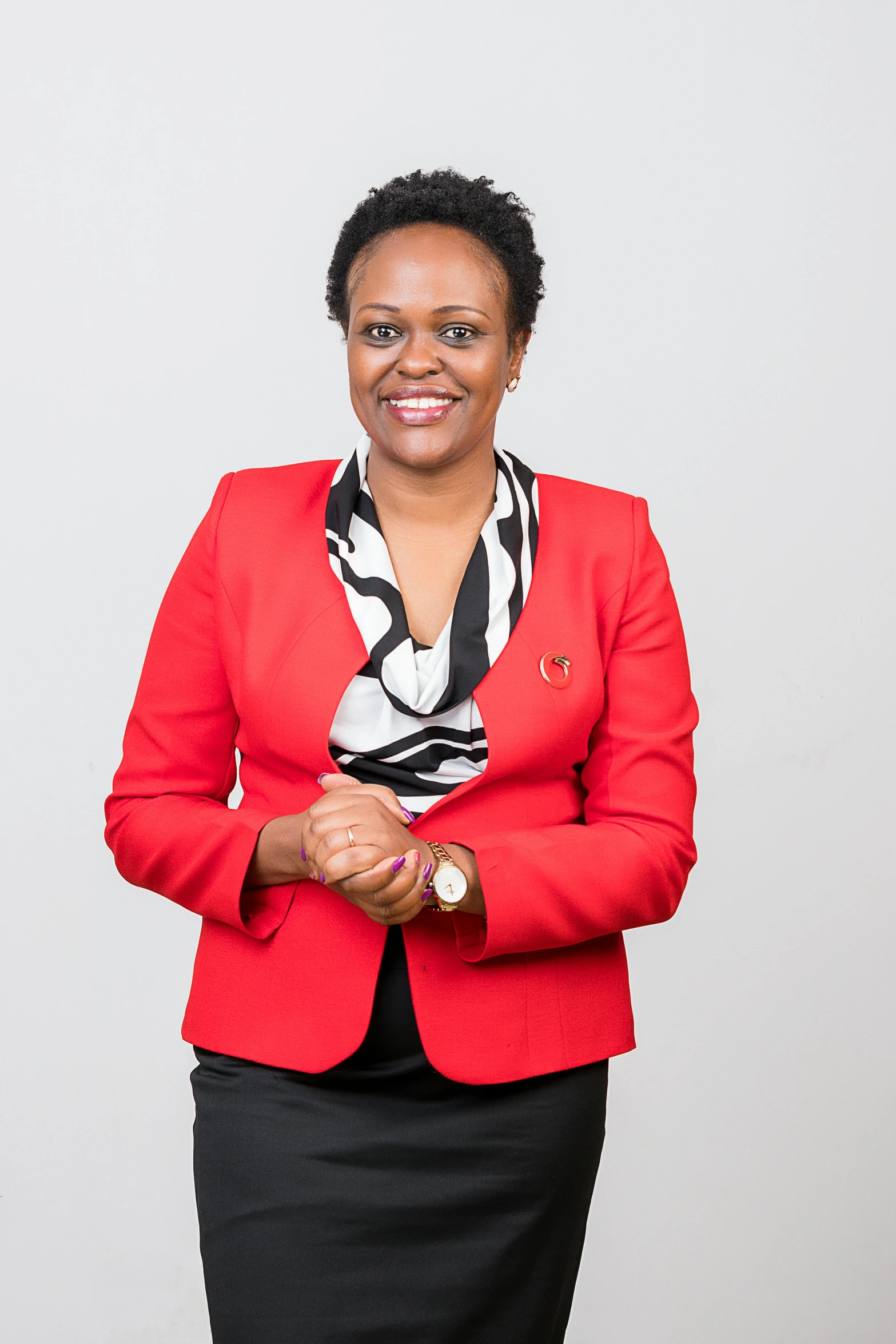 a woman with her hands folded wearing a red jacket and black skirt