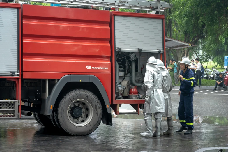 two firemen standing outside of a fire truck with an attendant