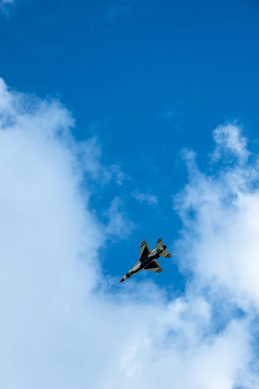 a fighter jet flying through a blue cloudy sky