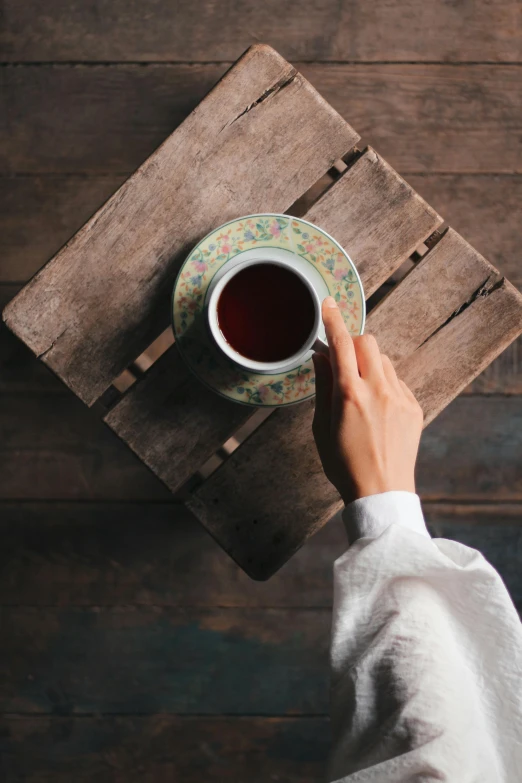 a person drinking tea from a cup near a plate on a table