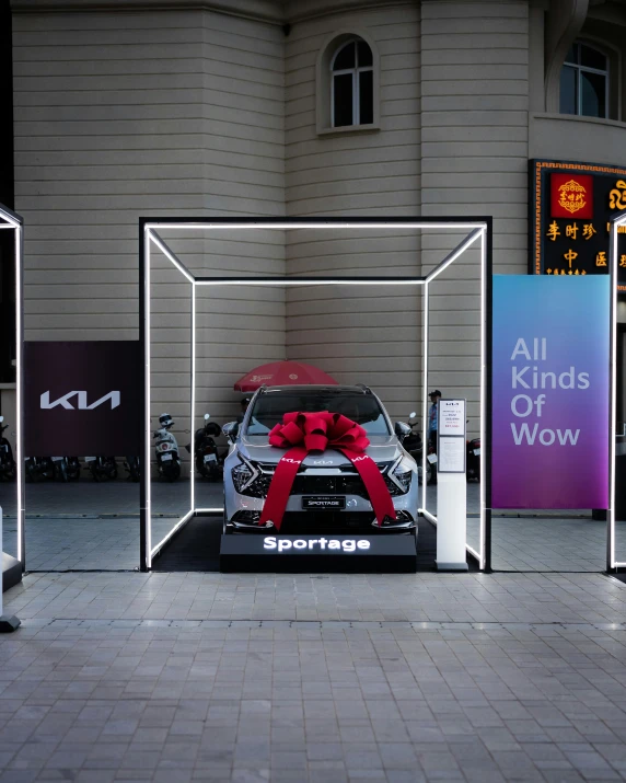 a car with a red bow on its tail is parked in an automobile show booth