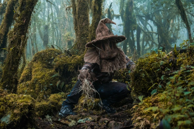 a person in a large hat and costume sitting in the middle of a wooded area