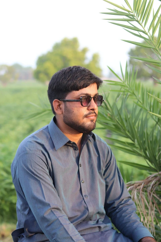 a man in sunglasses sitting outside next to a plant