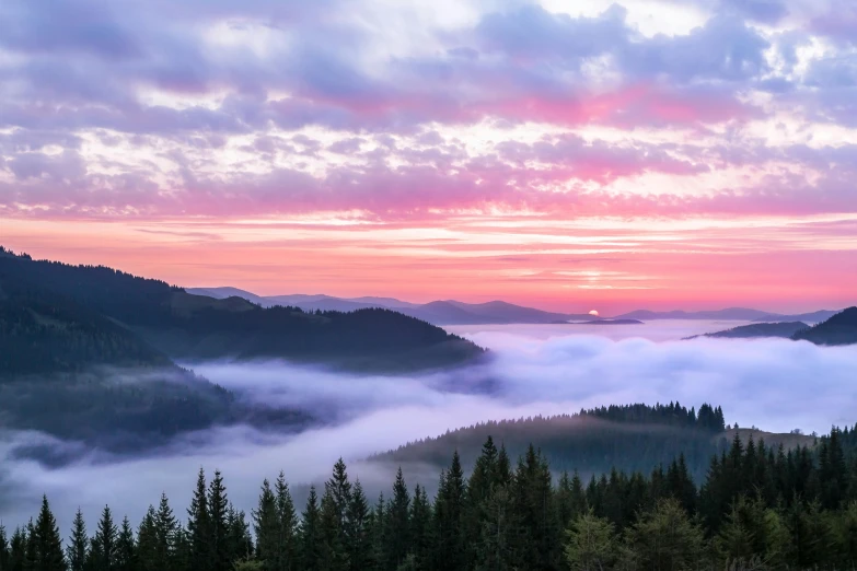 a view of mountains, clouds and forest at sunset