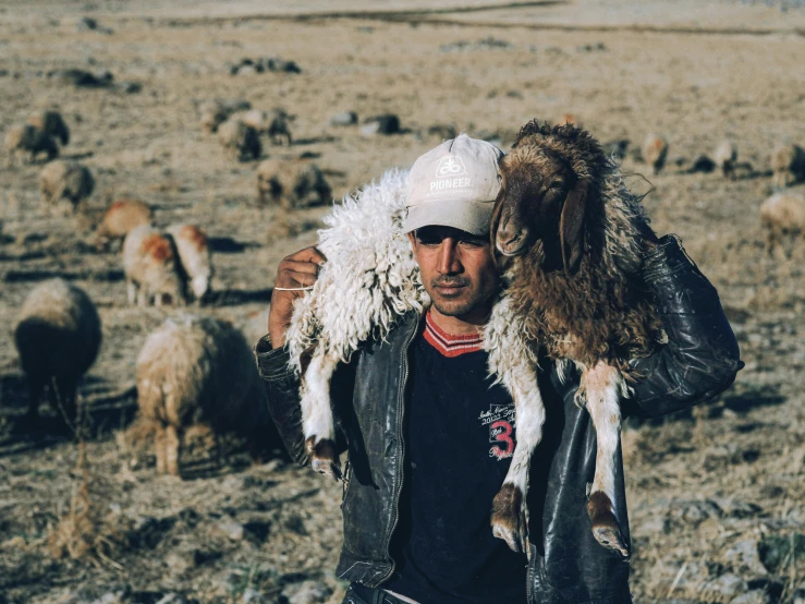 a man in a leather jacket and hat holding a goat