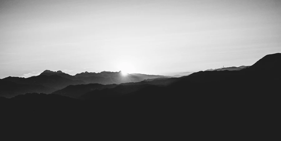 the sun peeking over the horizon in front of a mountain range