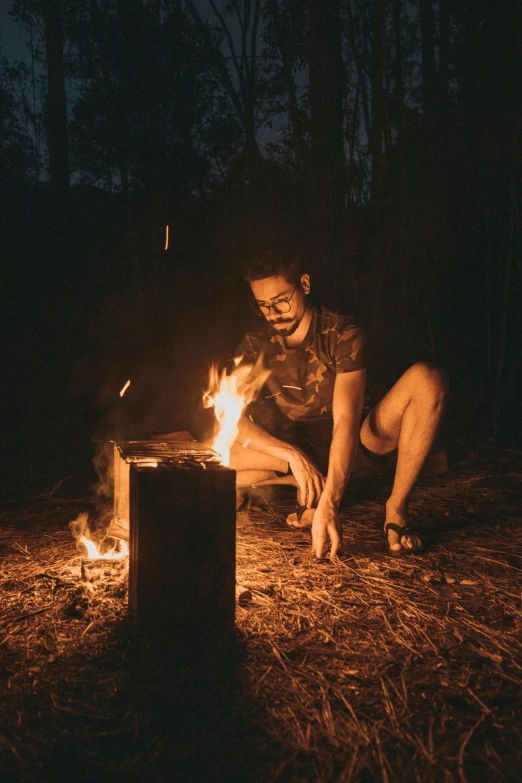 a man sitting in front of a fire next to a campfire