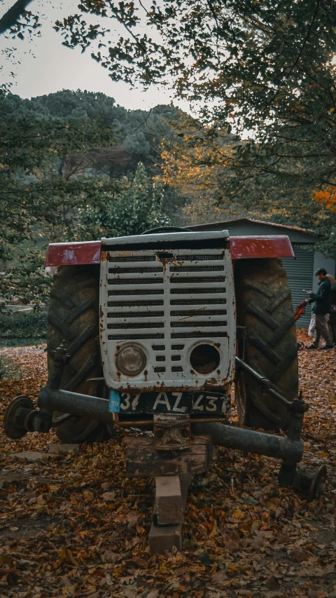 an old rusty, damaged tractor sitting in a patch of leaves