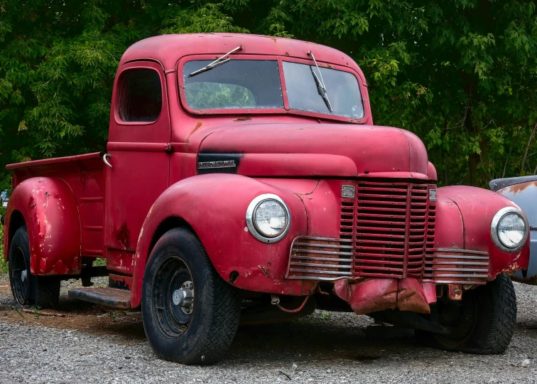 old and rusty red truck sits on the gravel